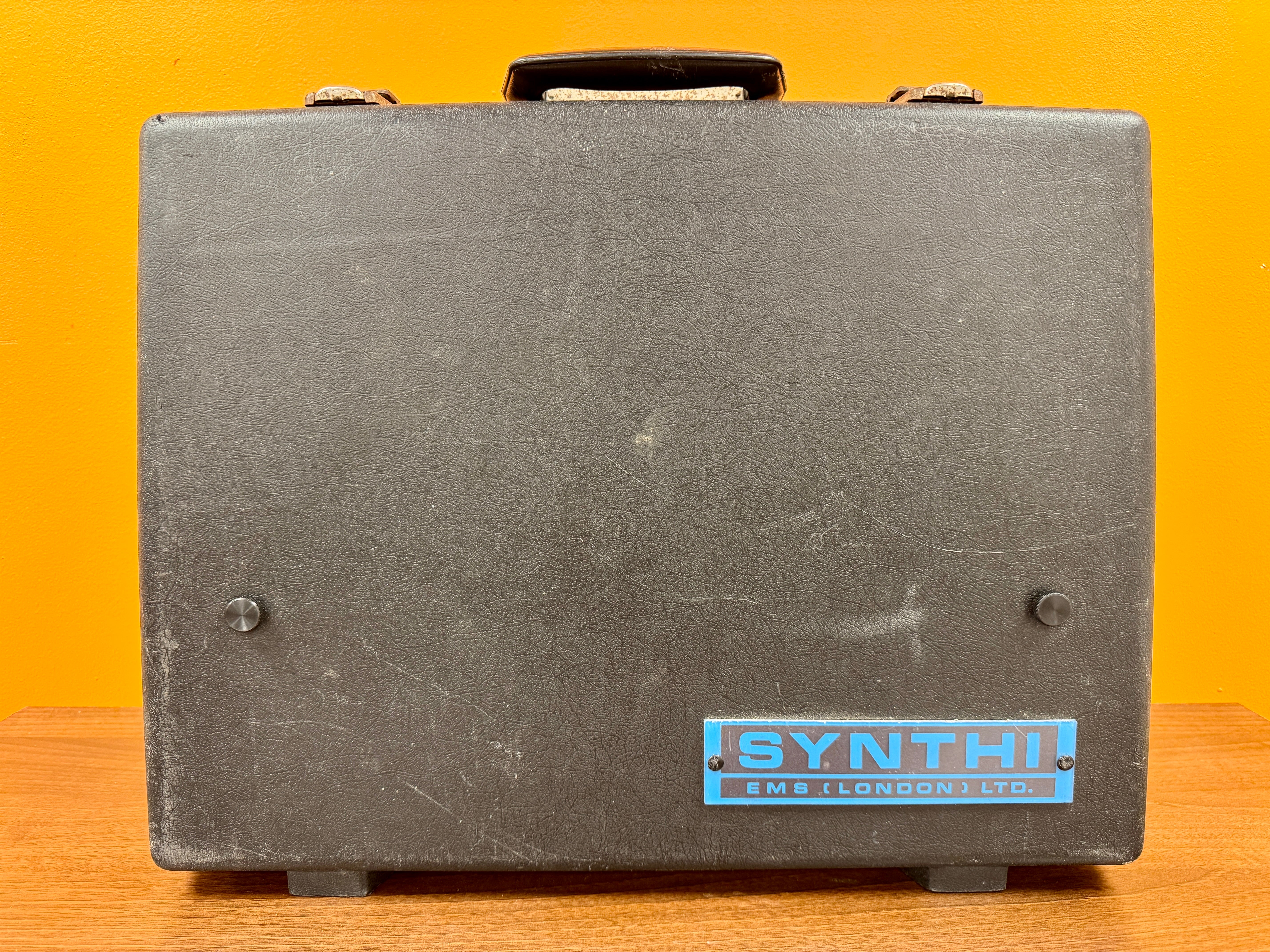 Vintage suitcase with 'Synthi' branding on a yellow background