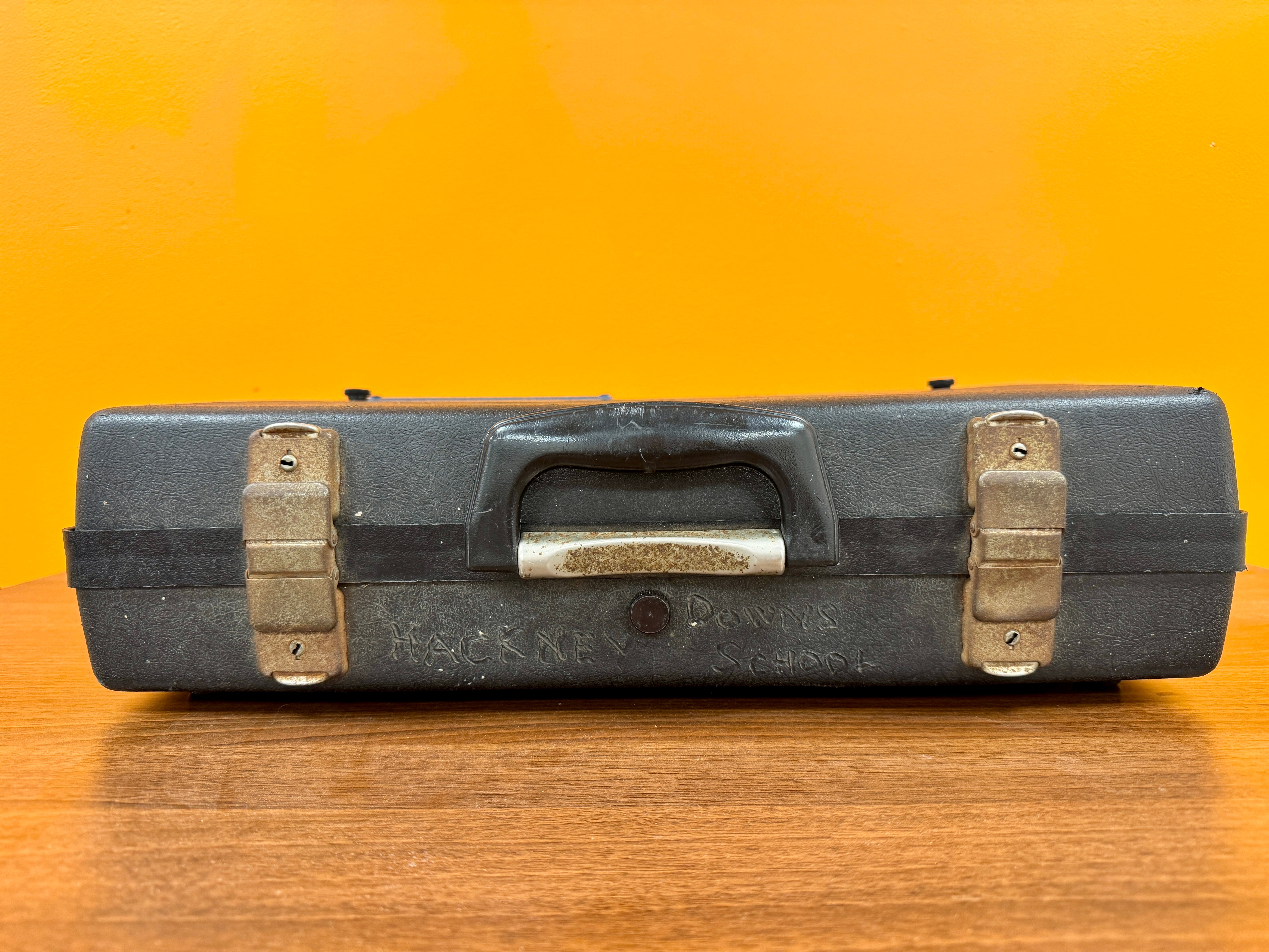 Black tool box with brass handles on a wooden surface and orange background