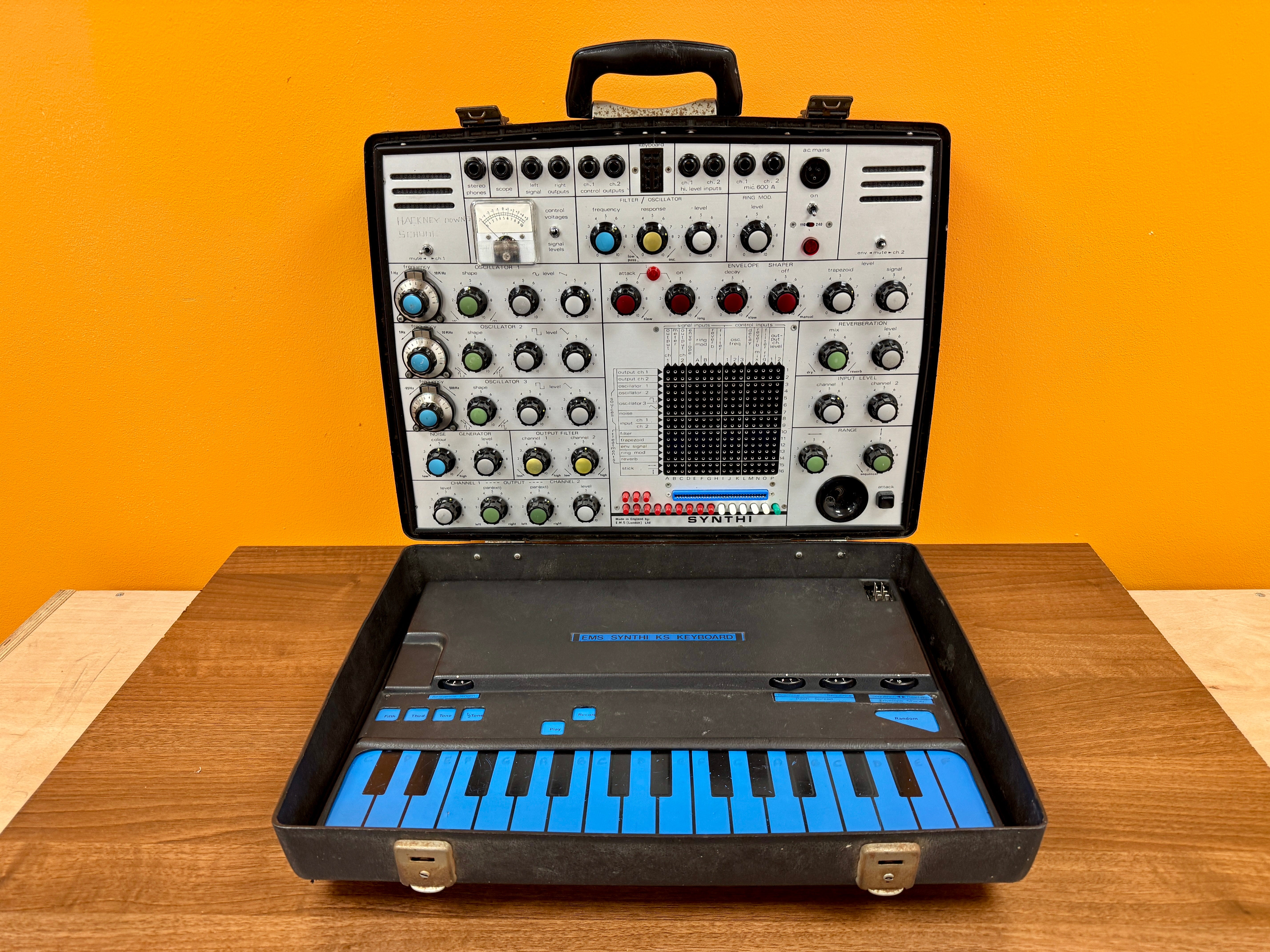 Electronic keyboard and synthesizer in a black case on a wooden surface with an orange wall background