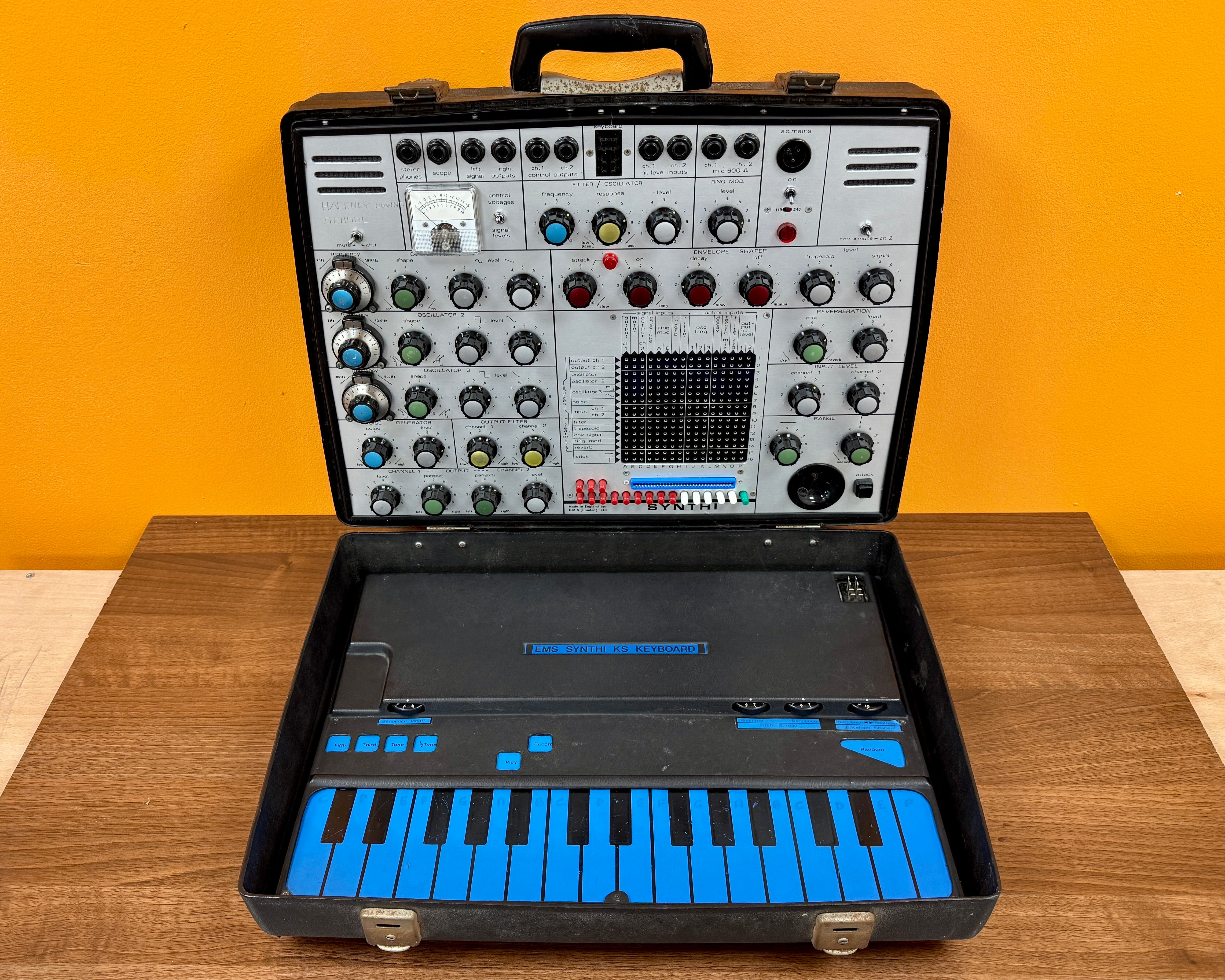 Portable electronic keyboard and synthesizer in a black case on a wooden surface with a yellow wall background.