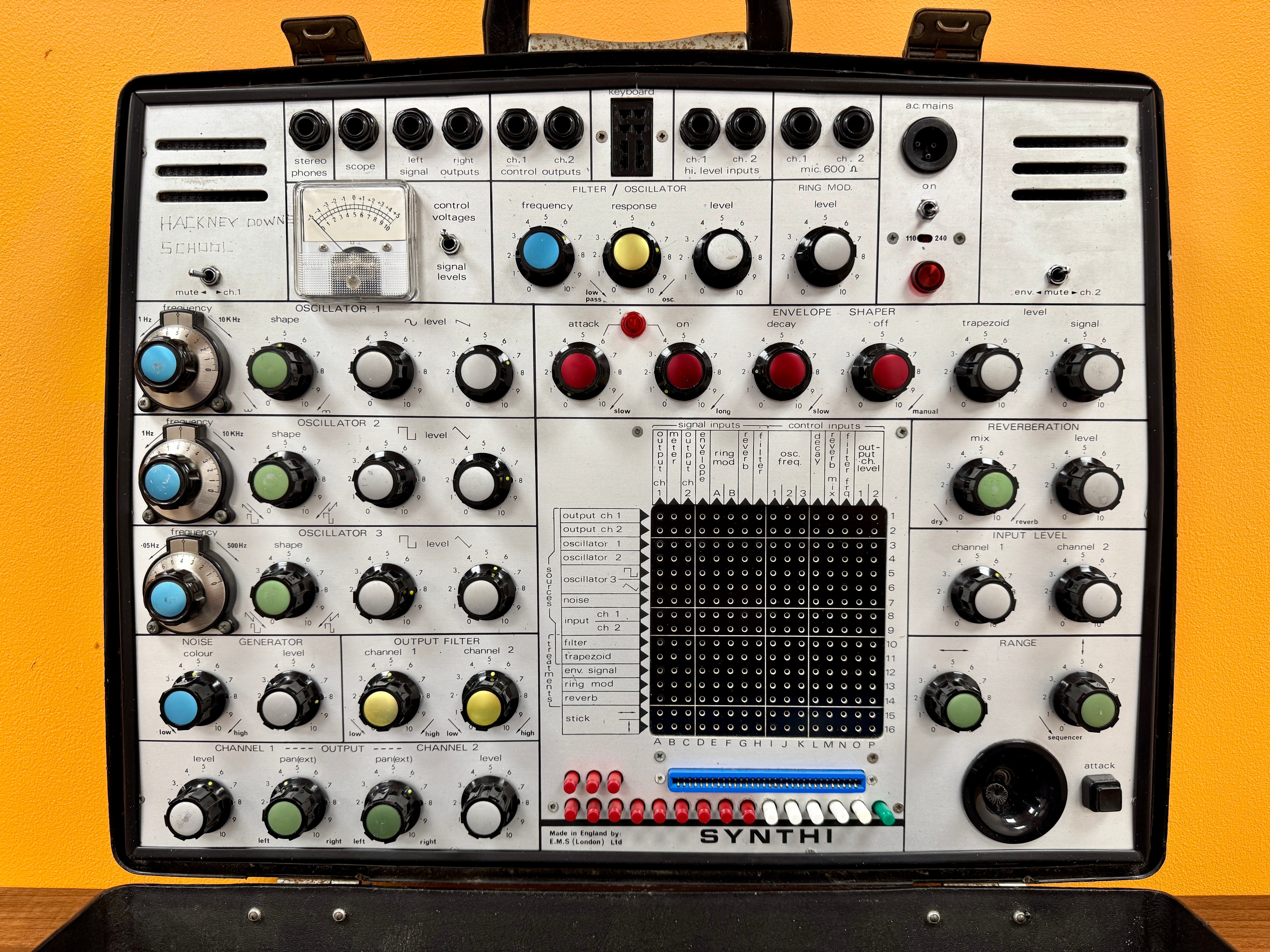 Vintage synthesizer with control knobs and buttons on a yellow background