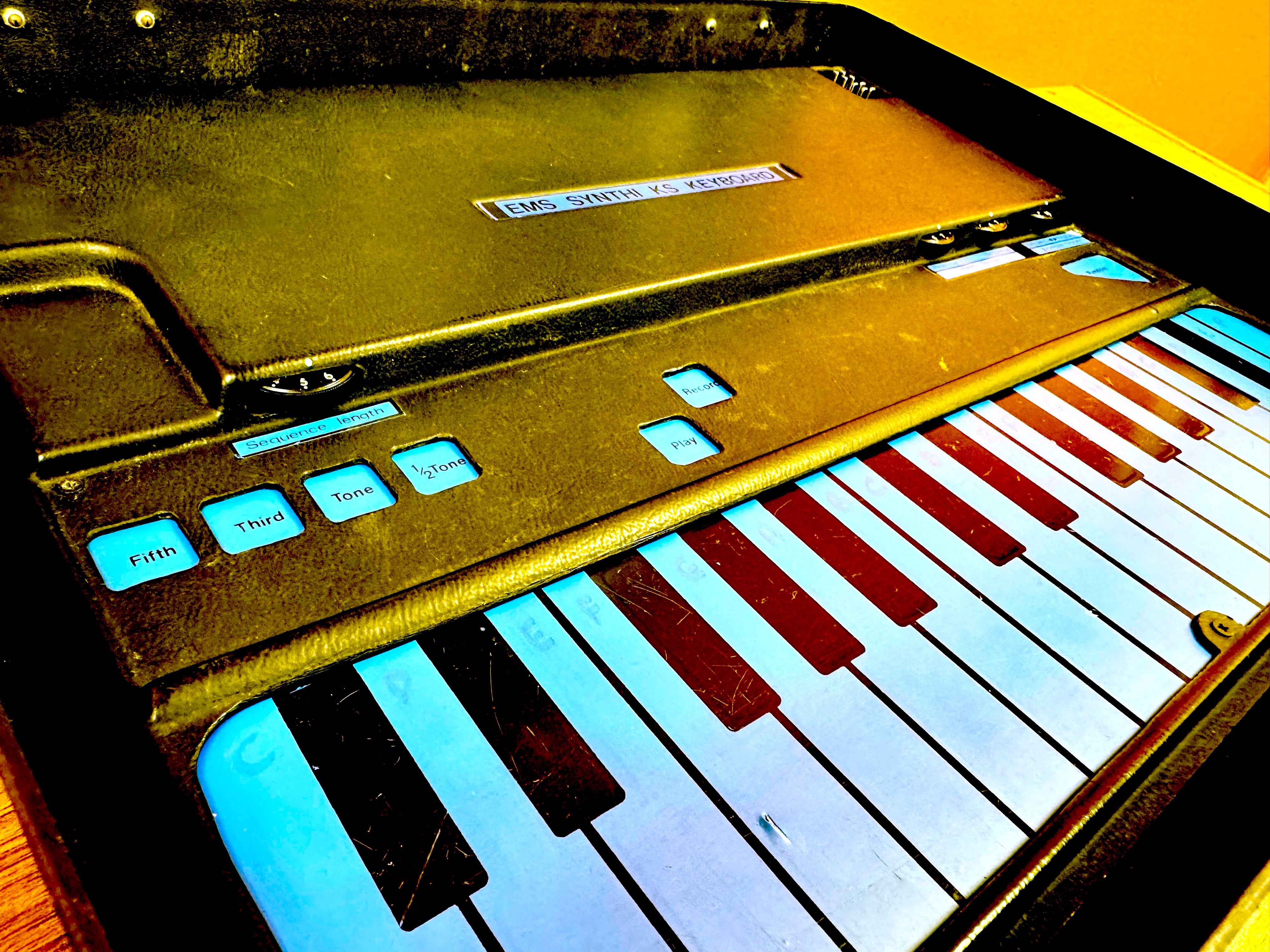 Small keyboard with gold casing and labelled 'EMS Synthi Keyboard' on a yellow background