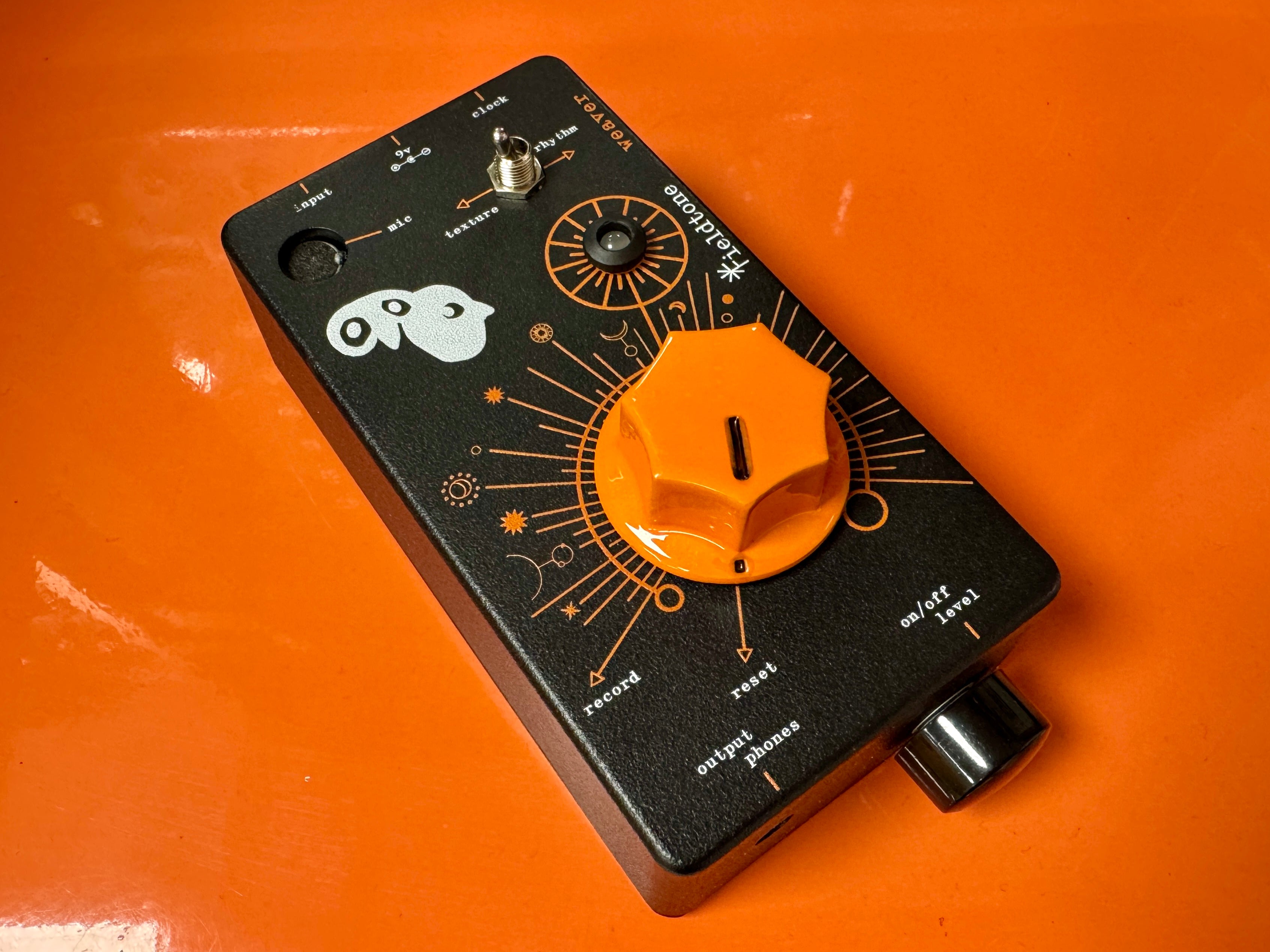 Black electronic pedal with orange knob on an orange background