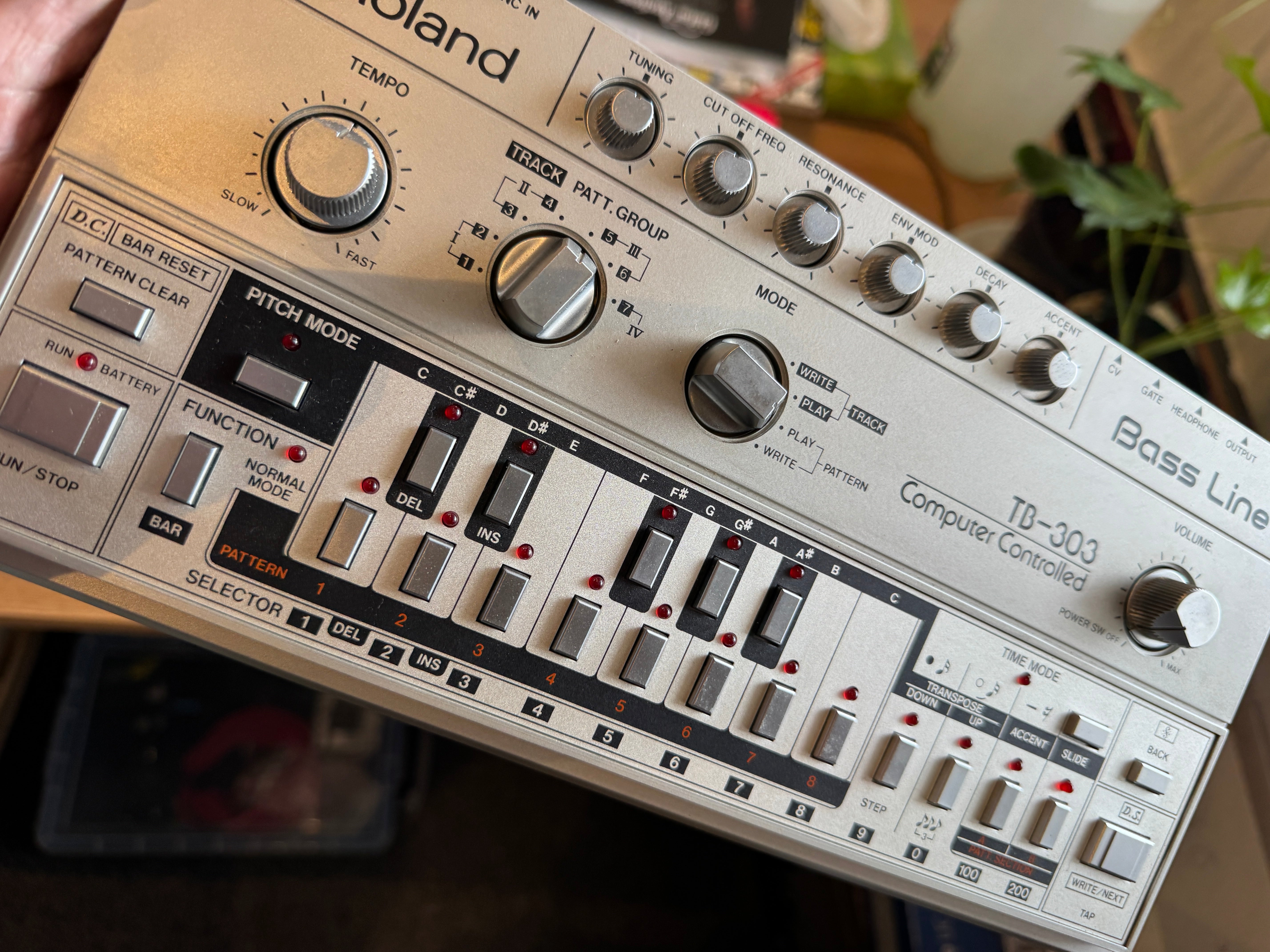 Roland TB-303 synthesizer with control knobs and buttons on a blurred background