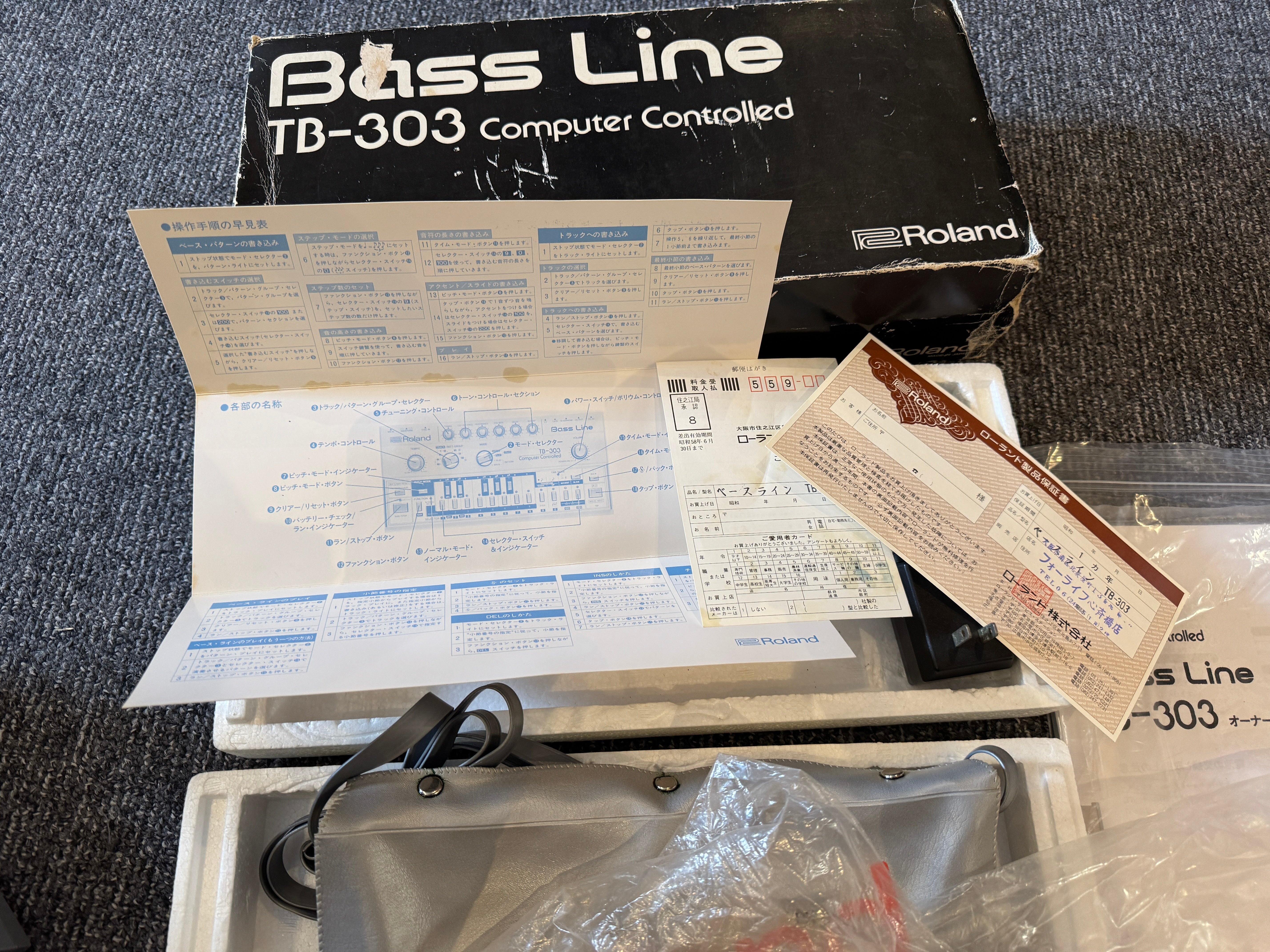 Roland TB-303 electronic keyboard with manual and documentation on a textured surface