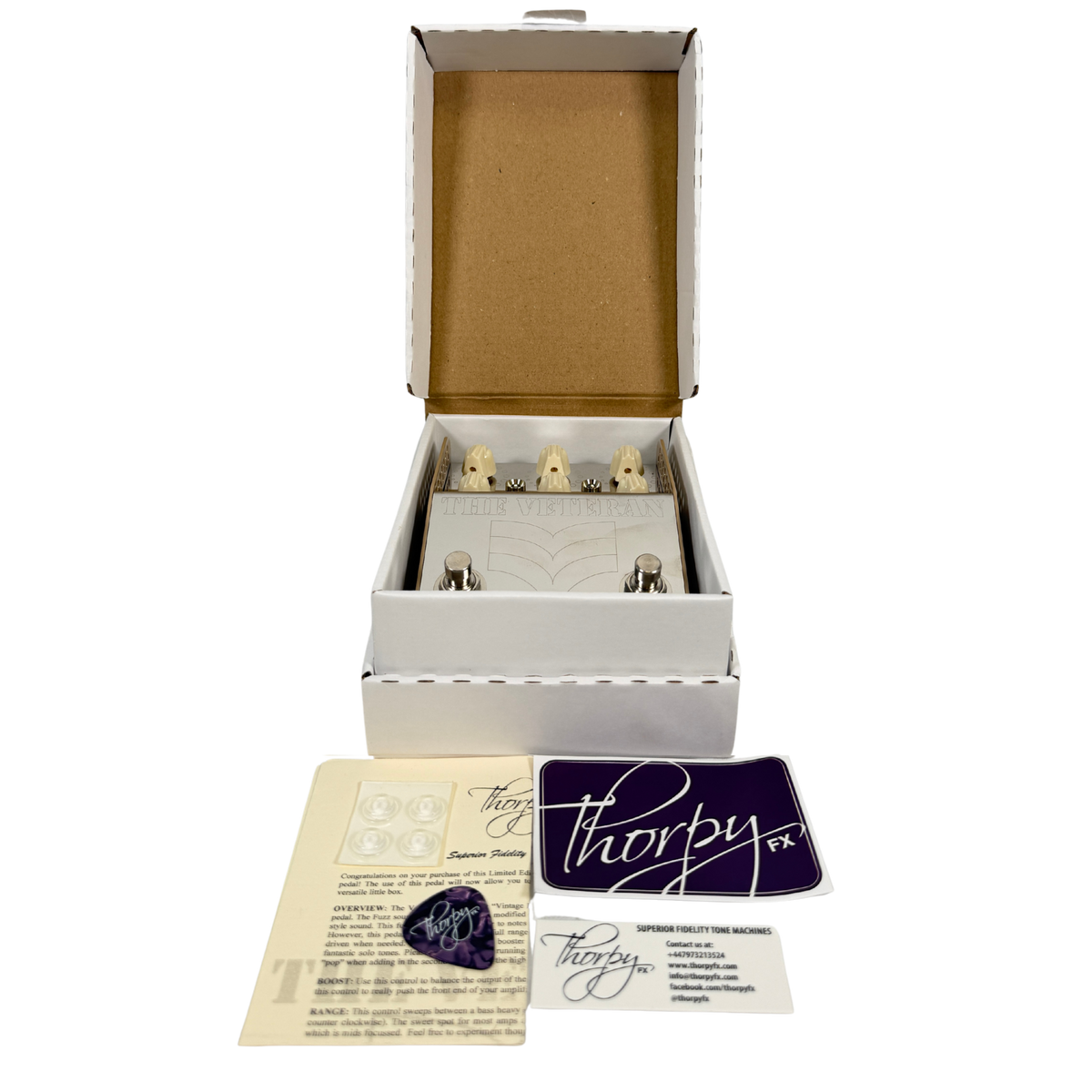A Thorpy FX guitar effects pedal set displayed in an open white presentation box with accessories arranged in front on a white background. The box is open to show the pedal inside, with printed cards and a purple Thorpy logo card placed below.